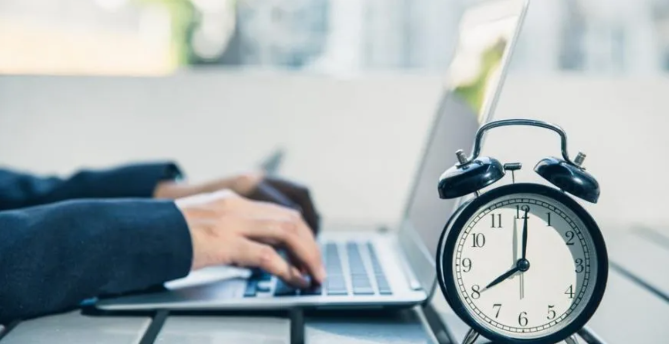 Realtor typing on a laptop in the background. With an analog clock in the foreground.