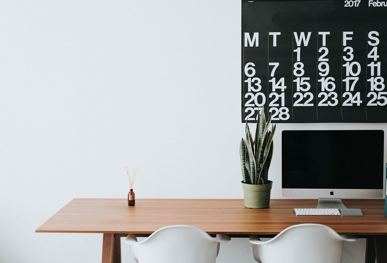 An office desk with computer and a calendar on the wall in the background