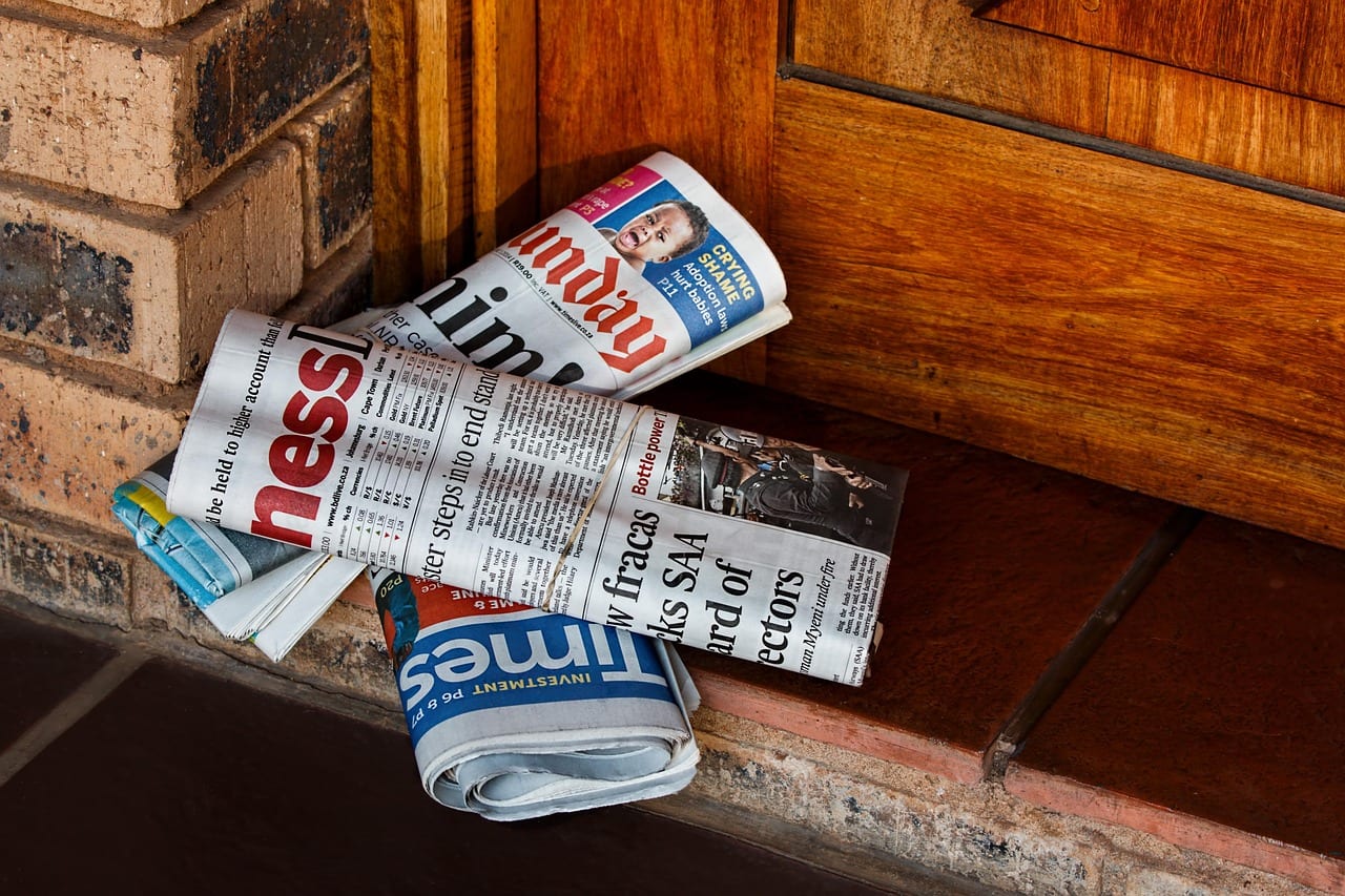 Newspapers bundled sitting in front of a residential front door.